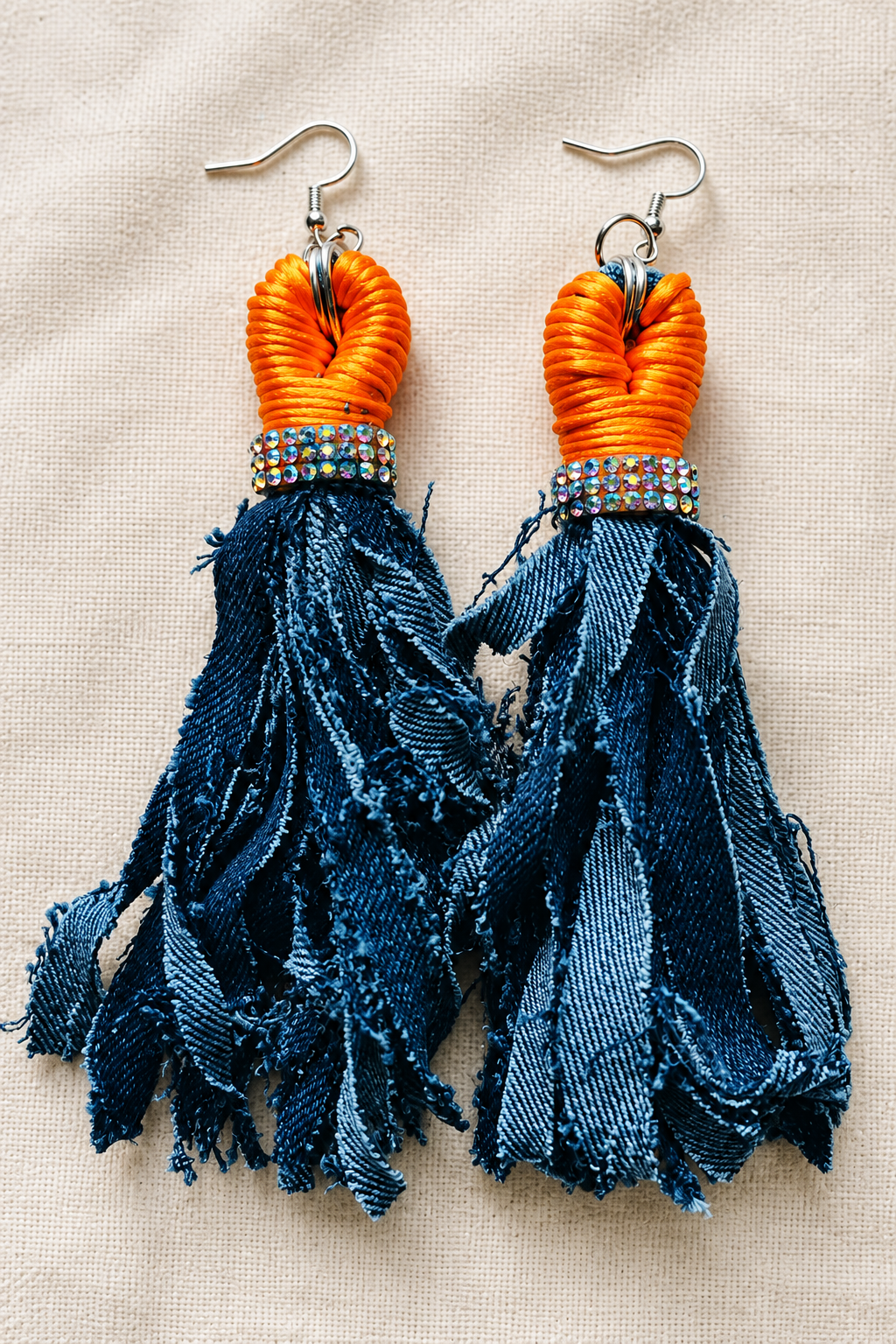 Close-up of orange and navy tassel earrings on cream fabric
