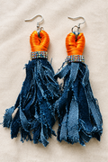 Close-up of orange and navy tassel earrings on cream fabric