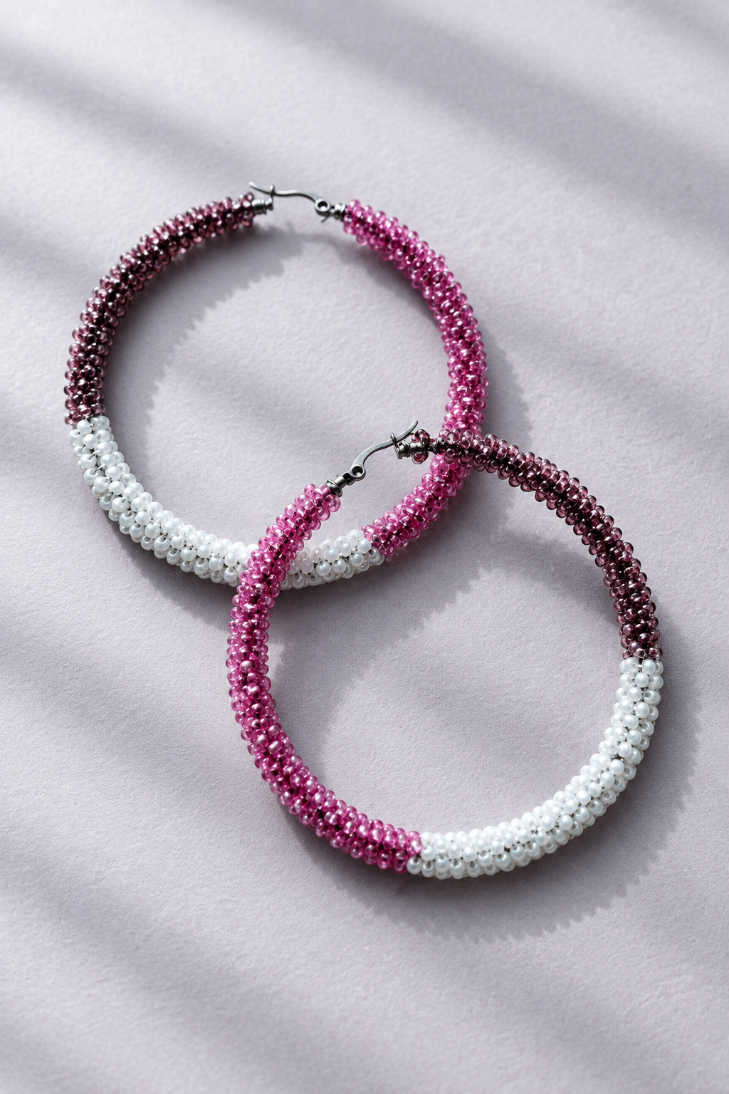 Pink, mauve, and white beaded hoop earrings on a gray-lavender background