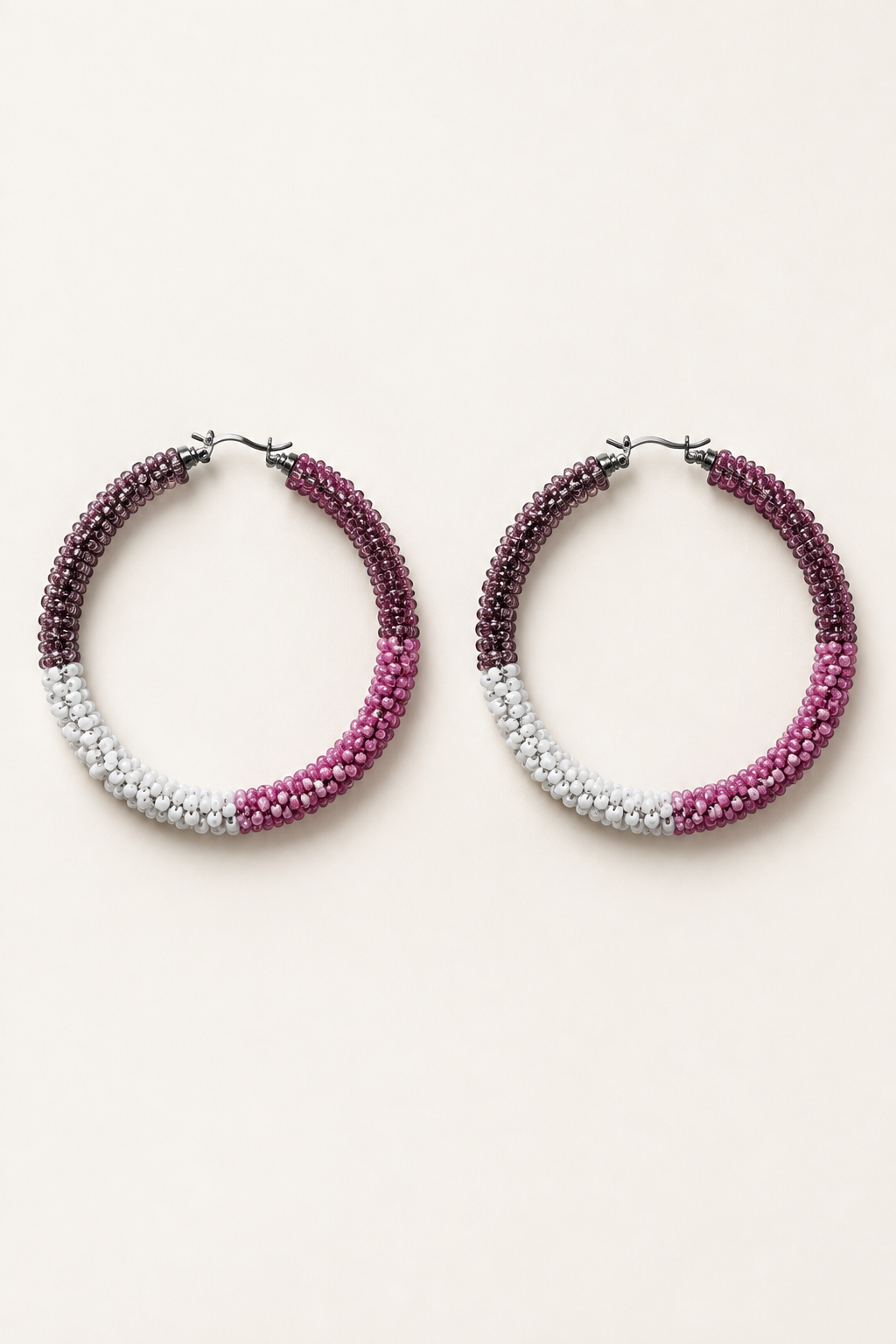 Pink, mauve, and white beaded hoop earrings on an ivory background