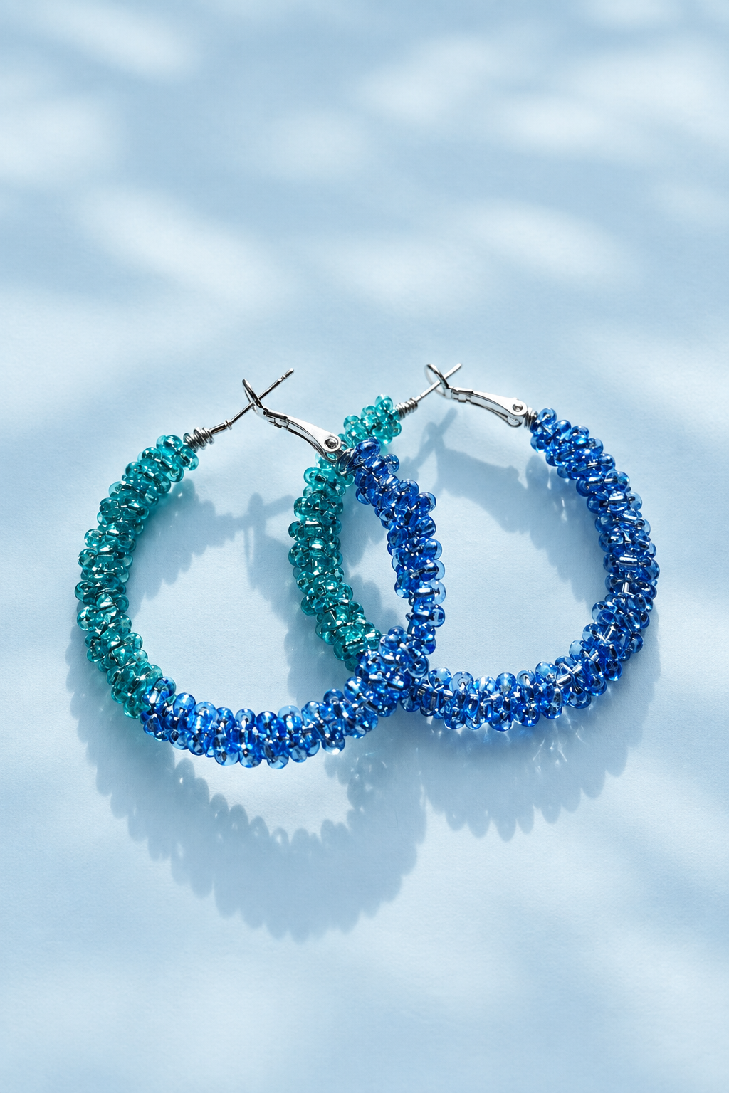 Teal and blue beaded earrings on a pale blue background